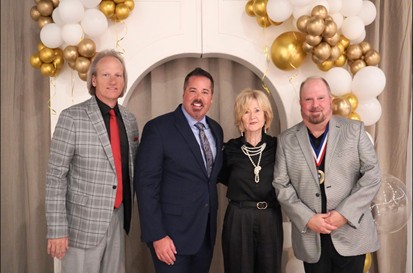 Chris Johns and three friends standing in front of a gold and white balloon arch